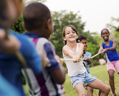 Happy school children playing tug of war with rope in park