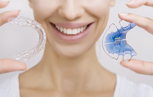 Woman holds up her retainer and Invisalign aligner