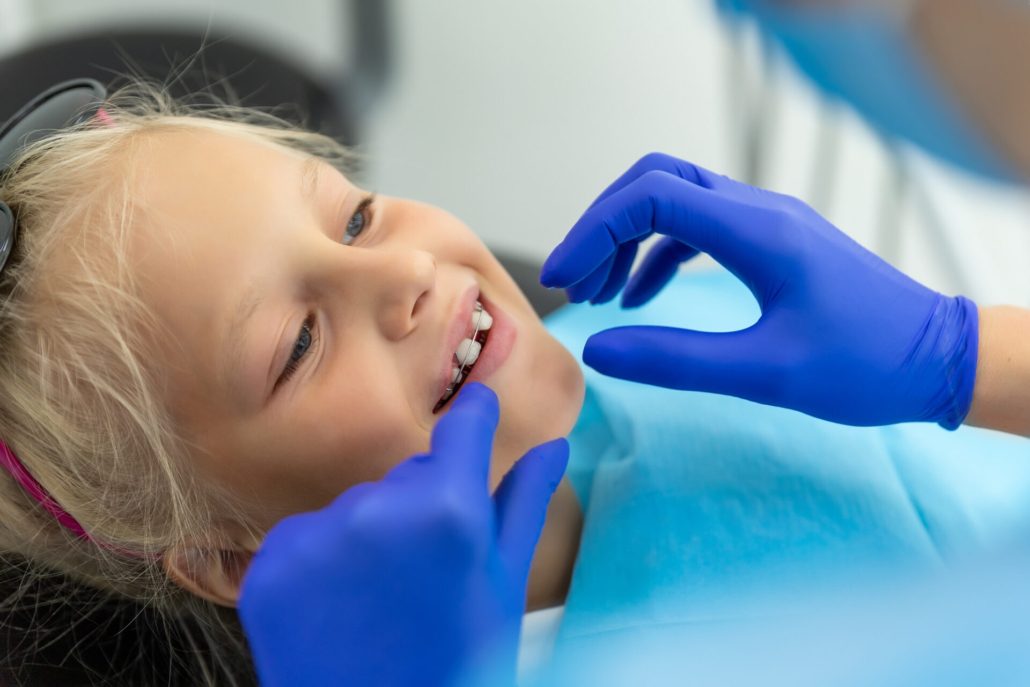Little cute adorable happy caucasian blond kid girl at dentist office at dentist check-up of dental braces. Child during orthodontist visit and oral cavity treatment. Children tooth care and hygiene